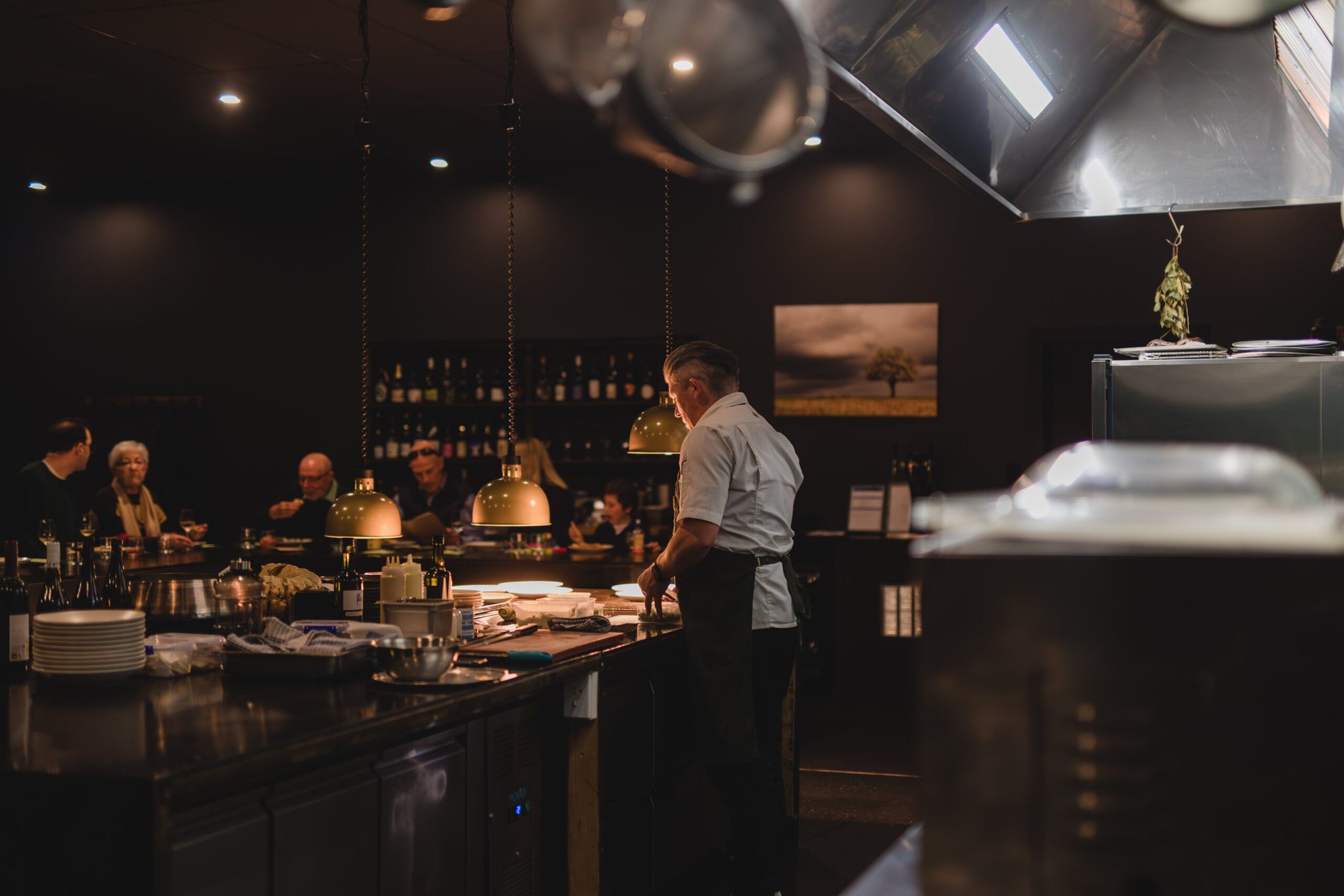 A Chef standing over a large kitchen bench in a dim lit restaurant