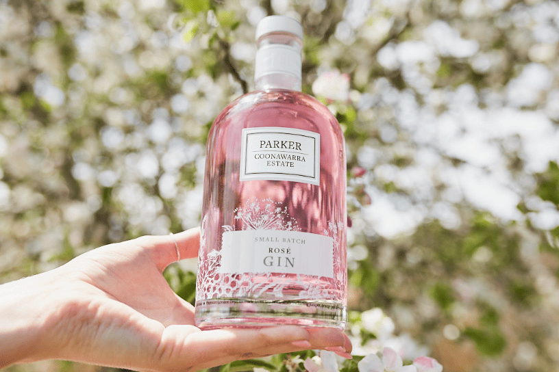 Hand holding a bottle of Parker Estate gin, outside in front of a tree.