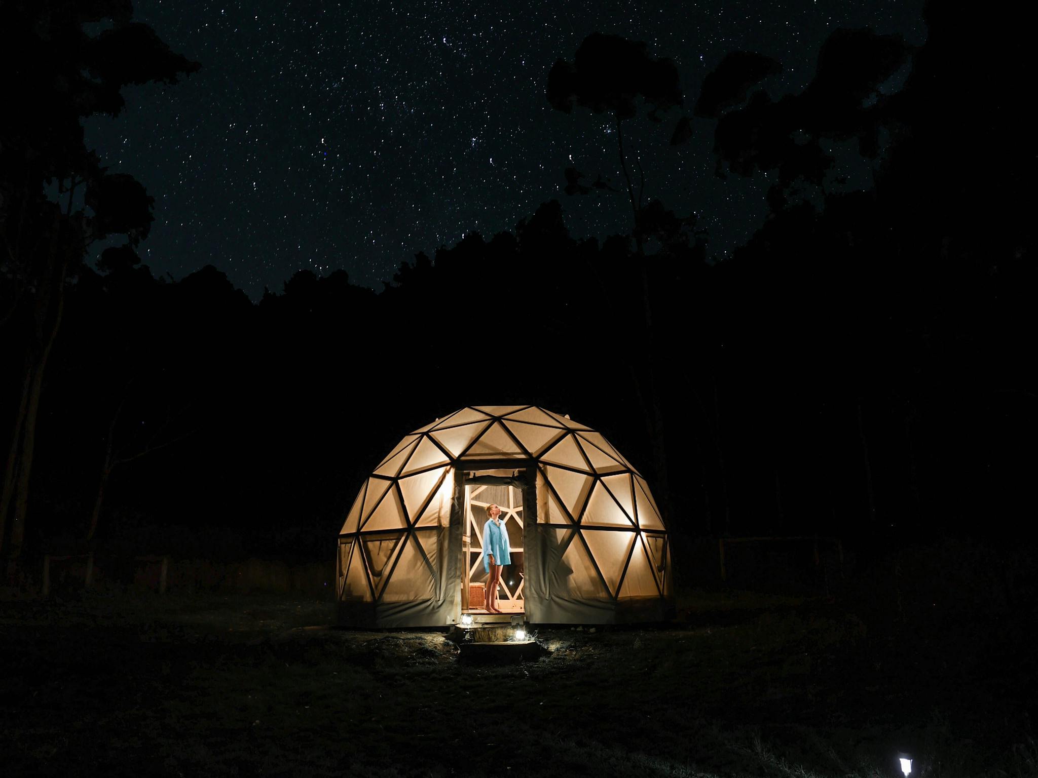 A geodesic dome aglow in the dark night amid a background of a starry sky.