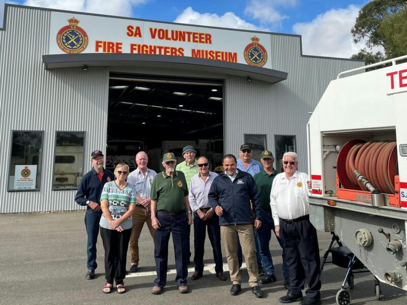 A group of museum volunteers stands in front of the Vehicle Pavilion with local MP