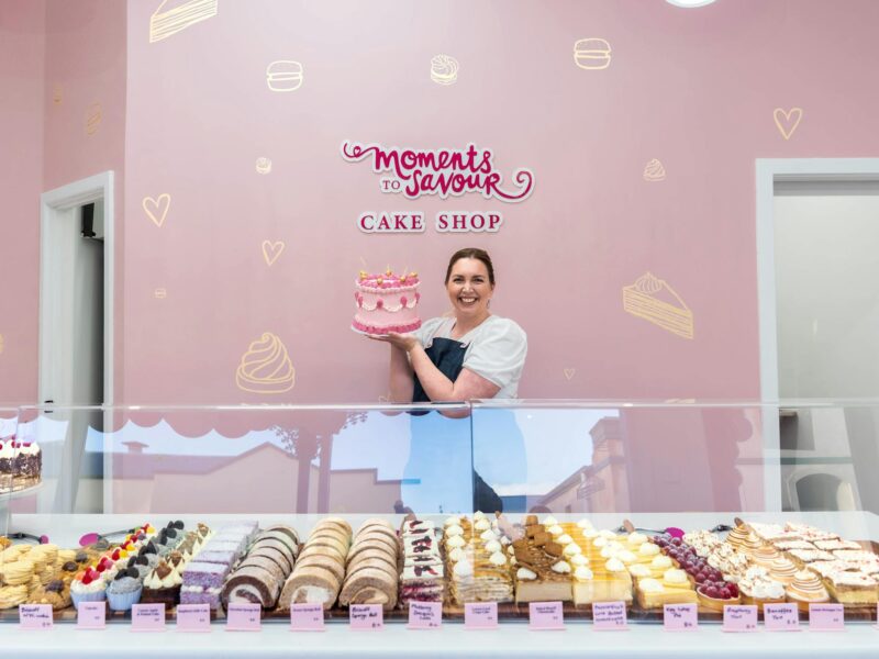 Sally holding cake in front of shop display