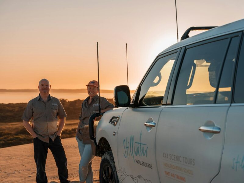 Tour vehicle on top of the dunes with owner operators standing next to it. Sunrise behind them.