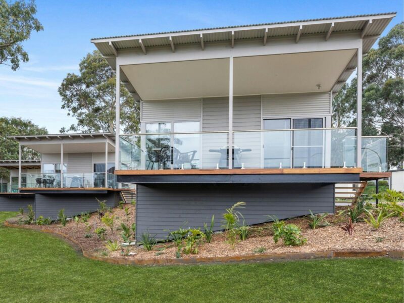 Villa with deck positioned above green grass and gardens