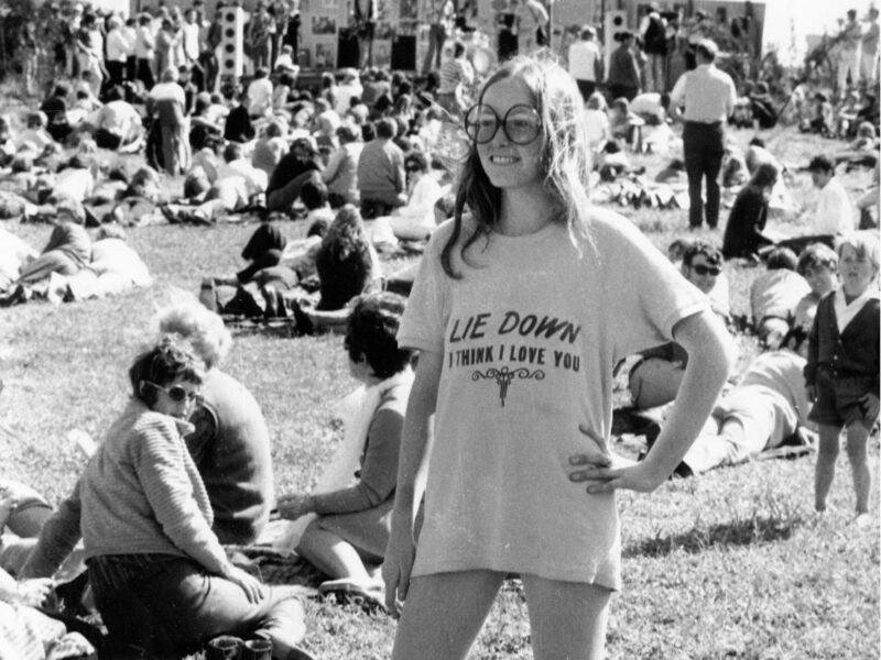 A black and white photo of a music festival with a young teen girl in the forefront with long hair