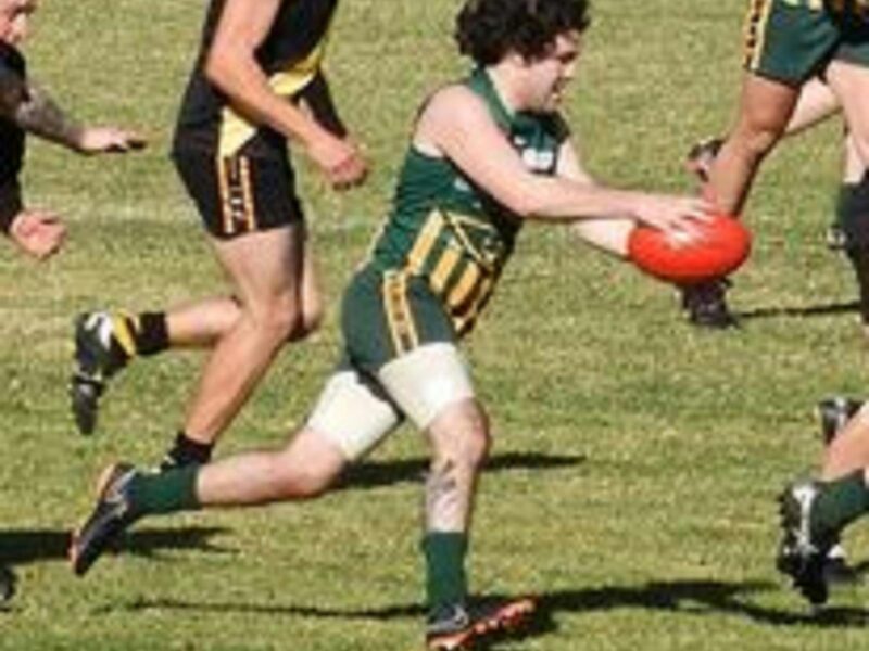 Man getting ready to kick the red football while he is running. He has short curly hair.