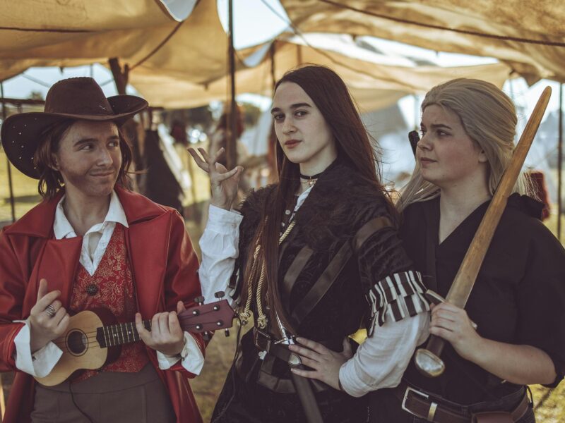 3 costumed people wearing Witcher costumes with props such as a ukulele and a sword.