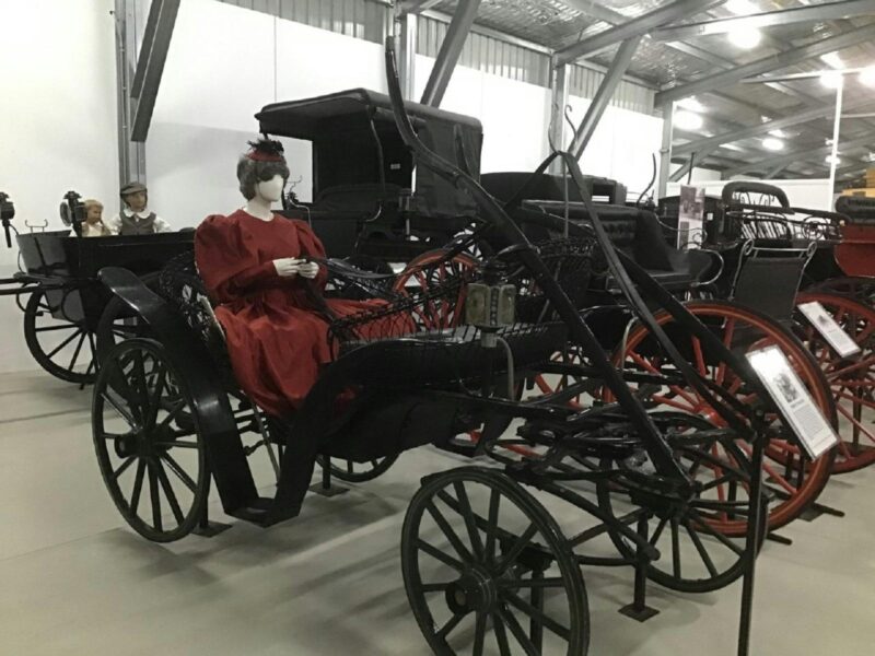 Beautifully restored black buggy with big wooden wheels with a mannequin dressed in red with a hat.