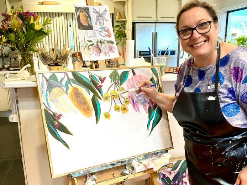 Cindy Bunt painting colourful gumnuts, yellow banksias and pink and grey waratah flowers.