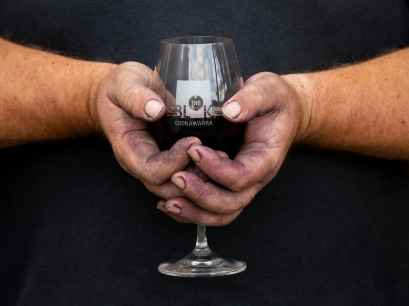 Red stained hands holding a glass with wine