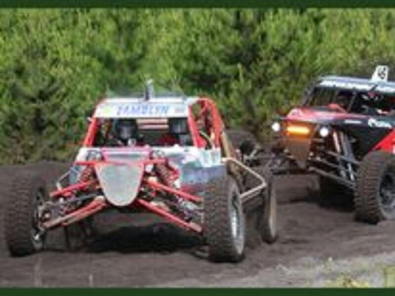 A red buggy competing in a race on a dirt track in front of another buggy with lights on.