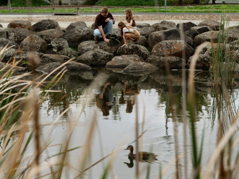 ATDW Mount Gambier Railway Lands.jpeg Family sitting on rocks next to pond