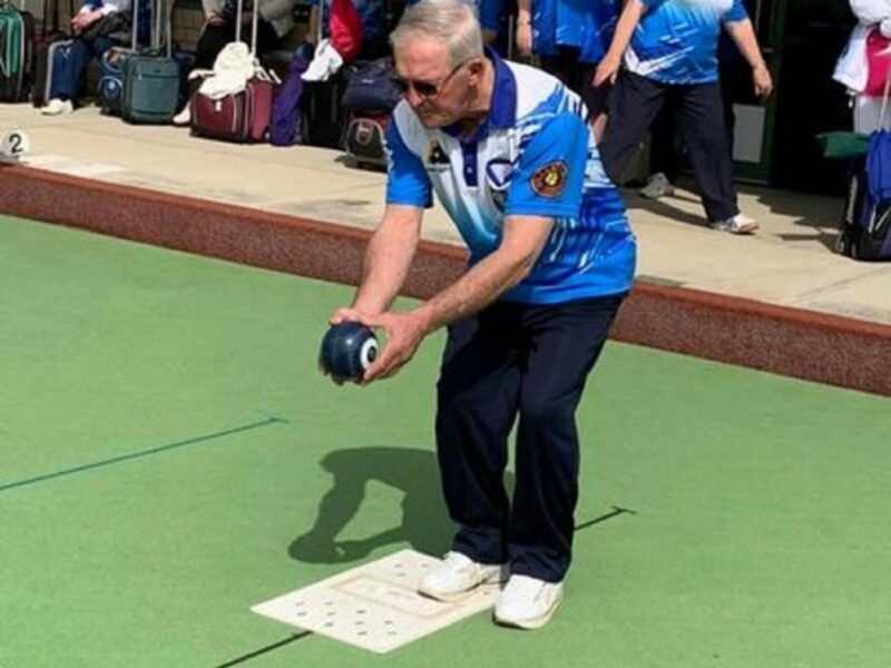 A man lining up with his bowling ball in his hand concentrating on sending his bowl down the lawn.
