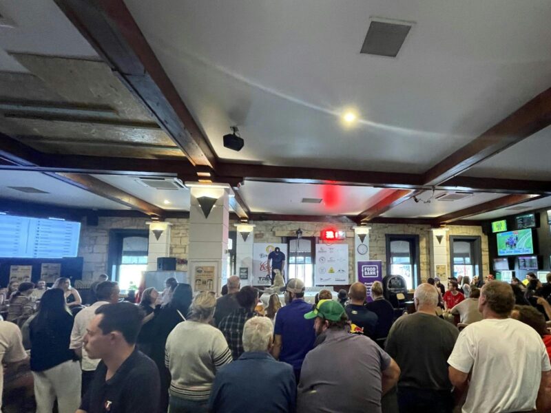 Shearer shearing a sheep in front of many people in a front bar of a hotel