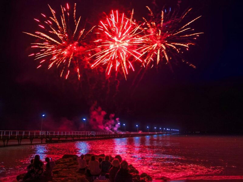A photo of orangey red fireworks pointing outwards, lighting up the sky near the Beachport jetty.