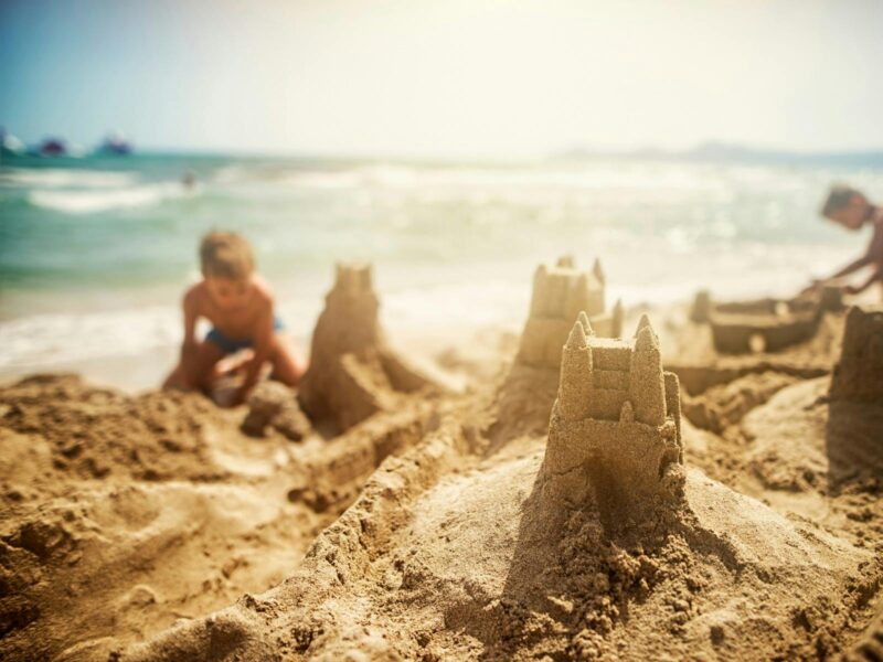 A photo of two children making sandcastles on the white sandy beach with the blue sea and white wave