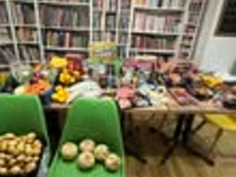 Two green chairs in a hall with lots of vegetables sitting on them. A table of more produce behind.