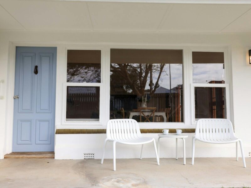 Front veranda with two outdoor chairs, a small table and the blue front door of the home.