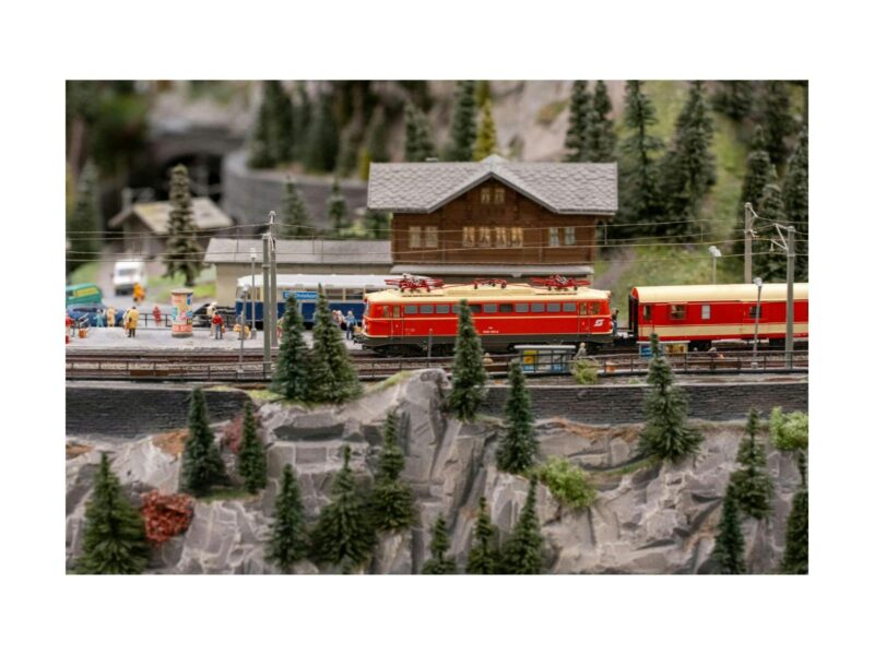 A model train display with a bright red train and carriages going past a railway station.
