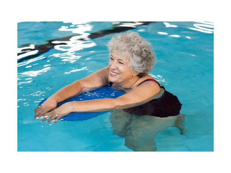 An older pretty lady with grey hair gently walking along the bottom of a blue pool on a blue board.