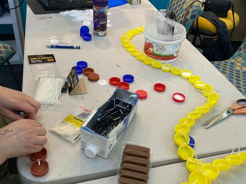 A line of yellow milk bottle lids all tied together making pretty artworks with them. Very effective