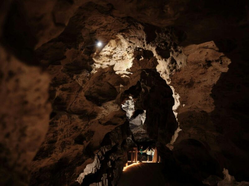 View looking down into Engelbrecht Cave, with rock illuminated and people standing in the distance