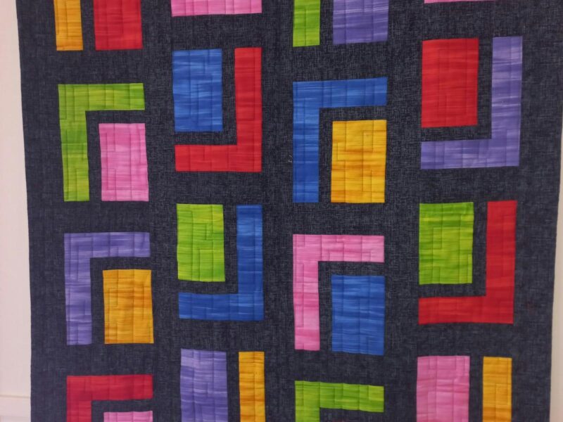A beautiful colourful quilt made of squares of blue, red, yellow and green on a black background.