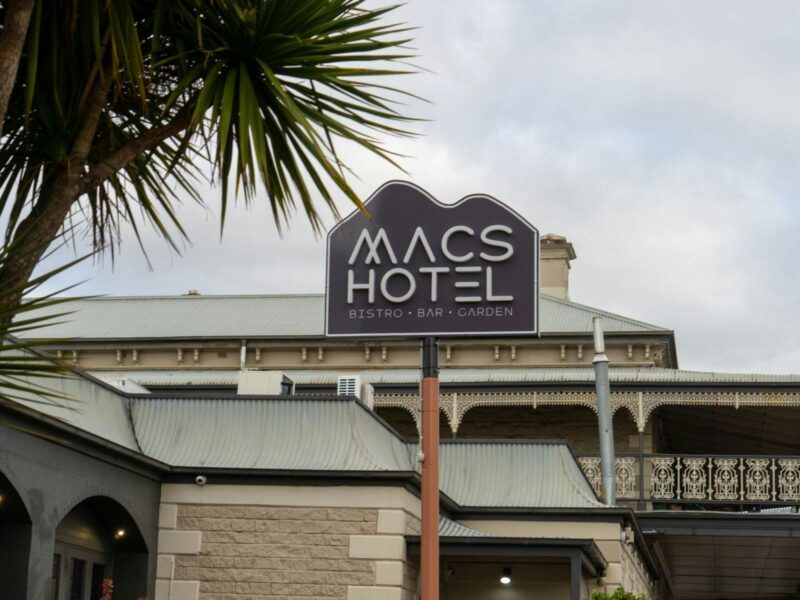Exterior view of Macs Hotel building with venue sign and palm tree in foreground
