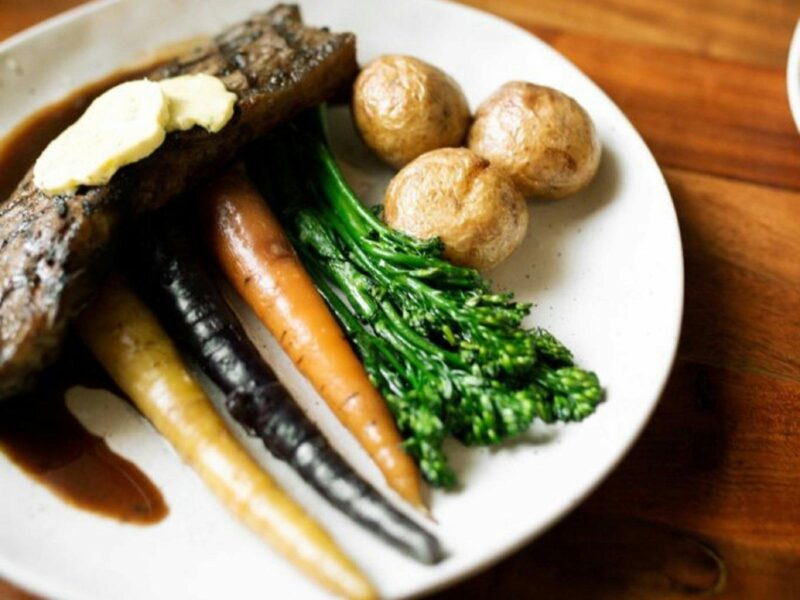 A plate of delicious steak with 3 potatoes, broccolini, carrot, parsnip and a black carrot and sauce