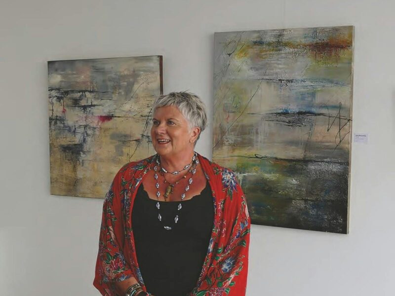 Juan posing in front of paintings. She is wearing a red wrap covering her black top with 3 necklaces