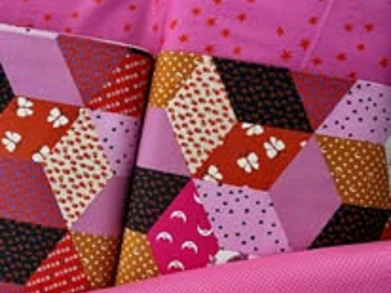 A beautiful bright fushia pink edged patchwork quilt with triangles in the centre with varied pieces