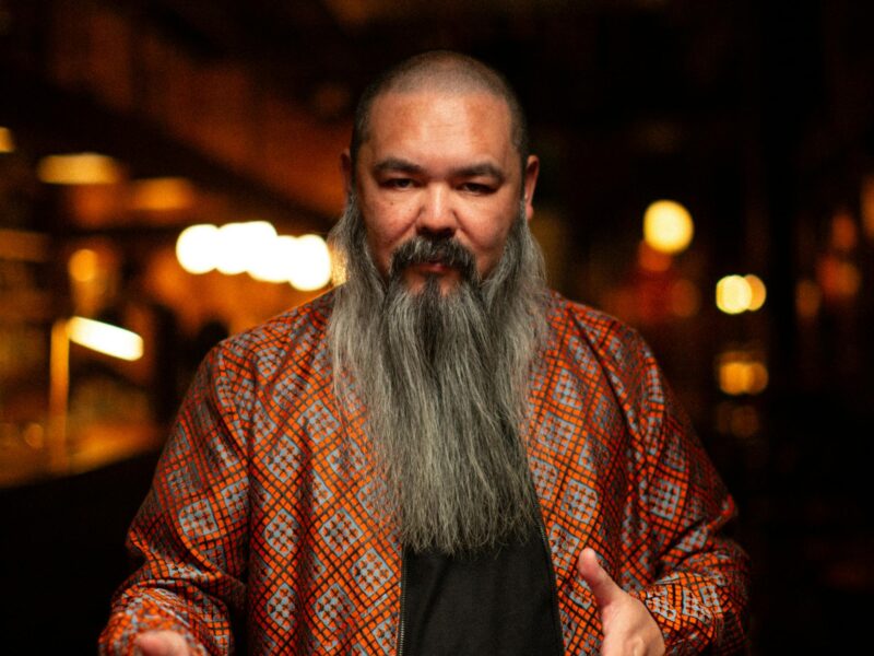 A man with dark skin and a long grey beard spreads out a deck of cards ready to perform magic