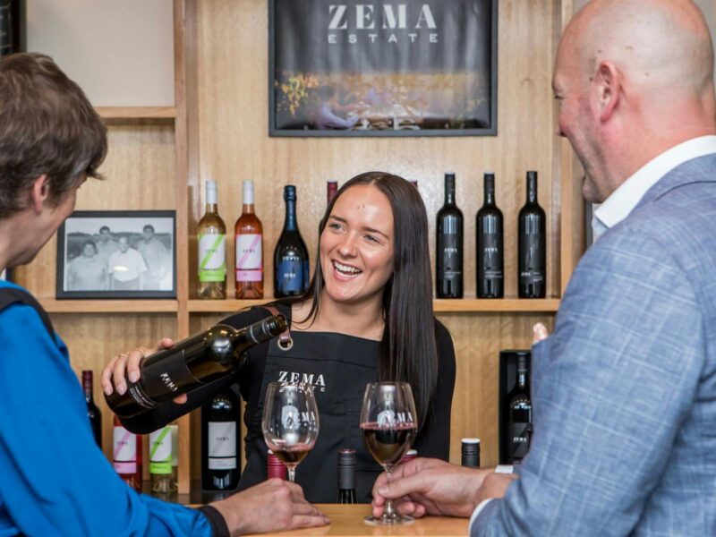 Young lady gives man and woman wine tasting in cellar door