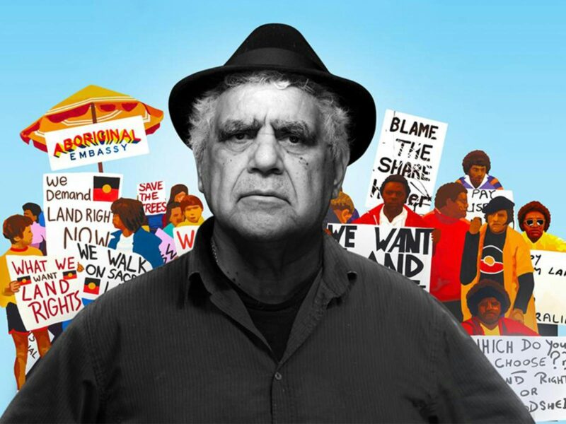 An elderly aboriginal man appears as a black and white photo in front of a colourful art collection